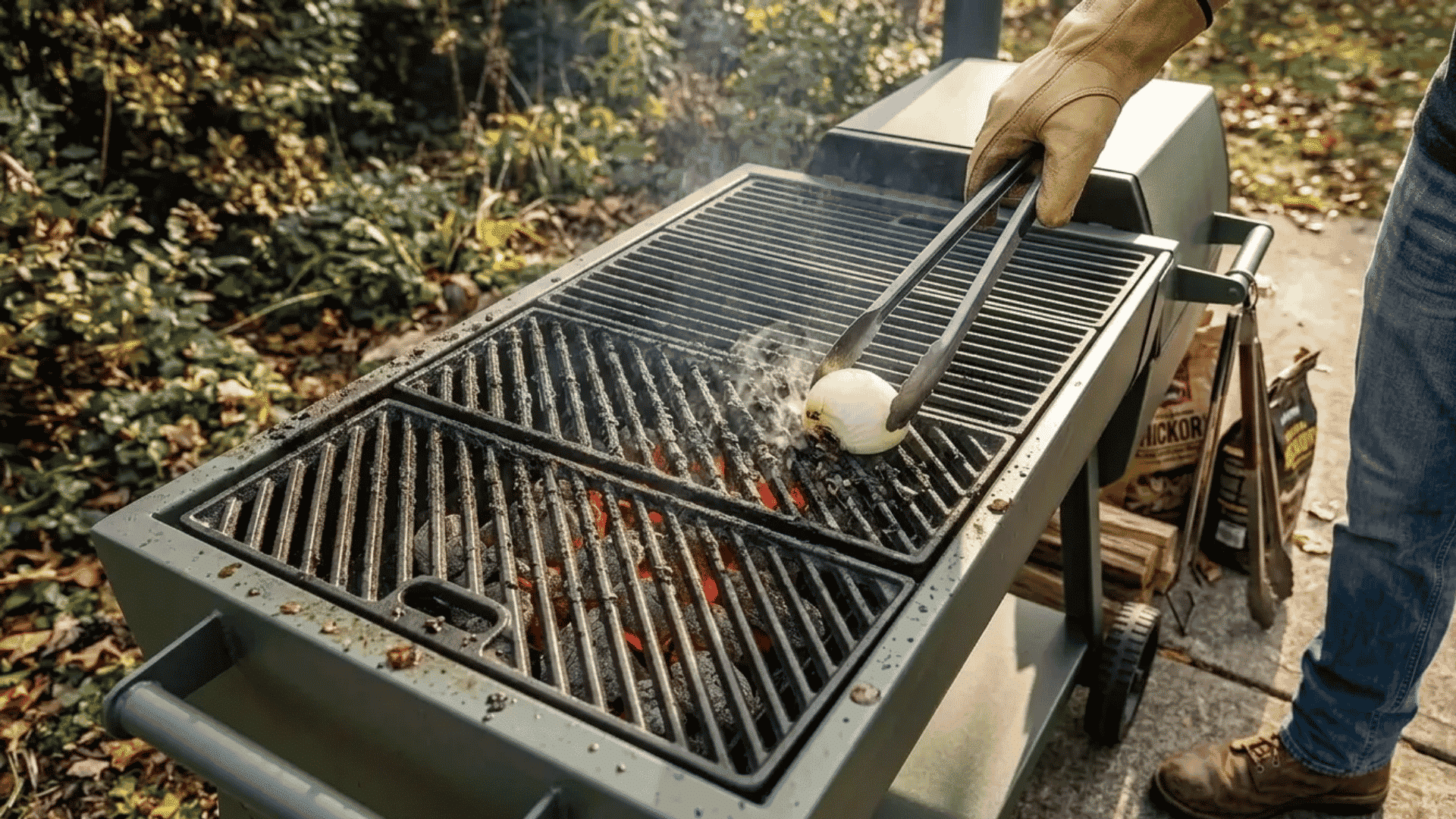 Person rubbing a cut onion across hot grill grates with tongs on an outdoor charcoal grill.