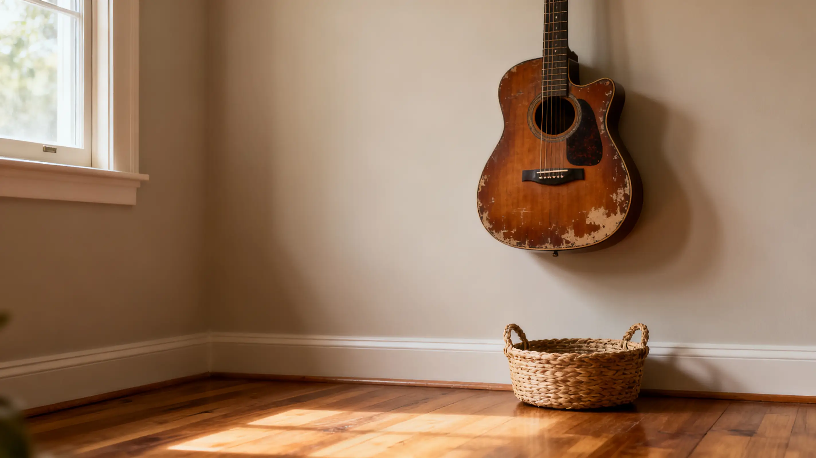 Acoustic guitar hanging on wall in sunlit room with woven basket on hardwood floor