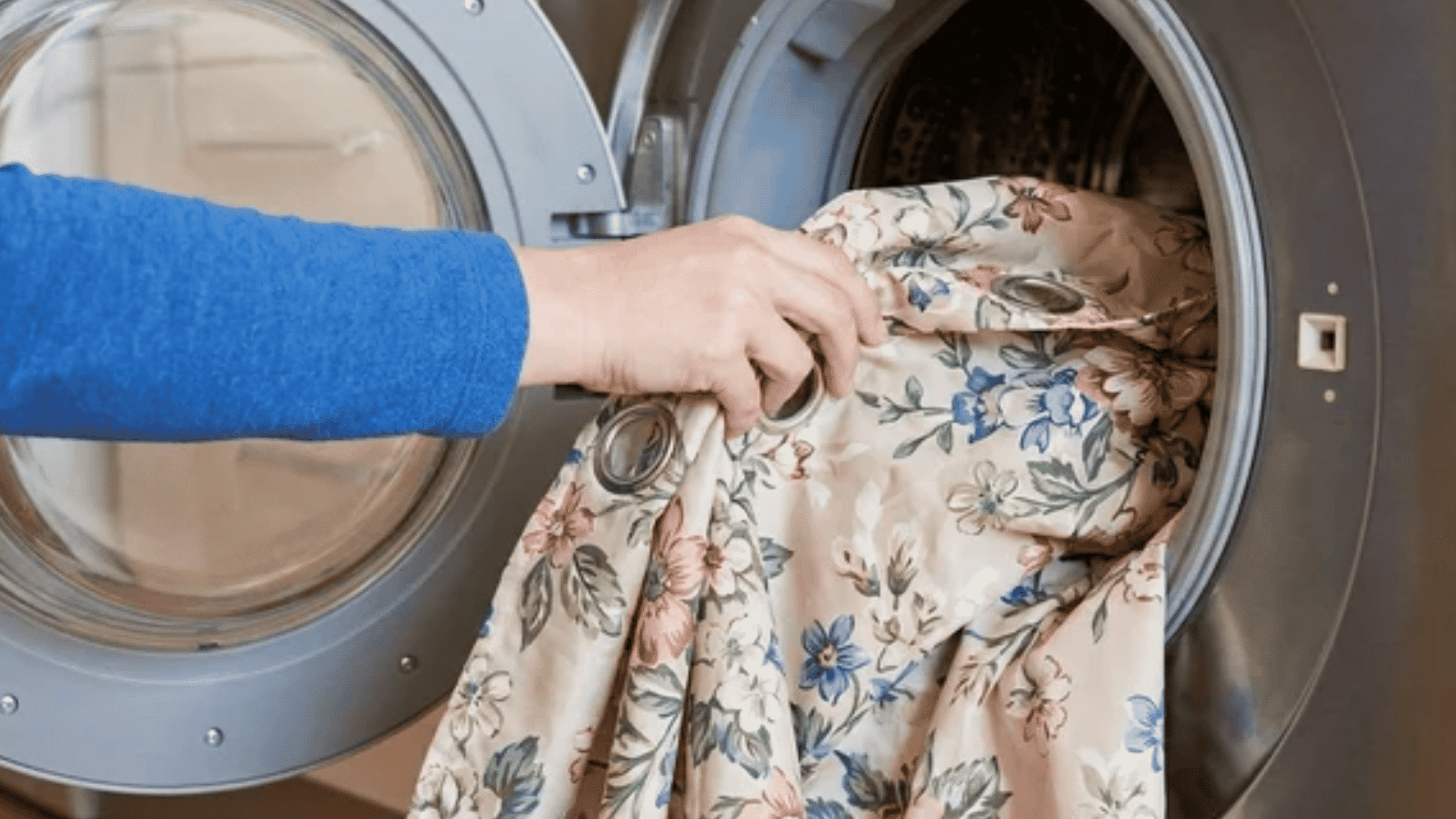Hand placing a floral shower curtain into a front-load washing machine.