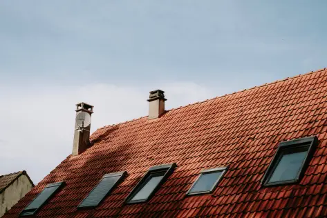 Red tiled roof with chimneys and skylights under clear blue sky