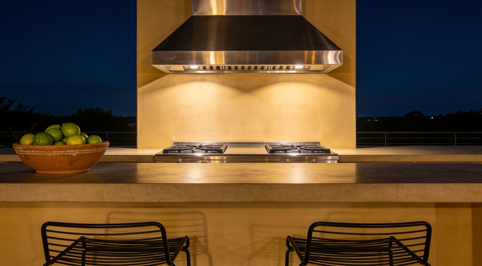 Outdoor kitchen counter on a covered deck at night with warm LED toe-kick lighting washing softly across the floor below