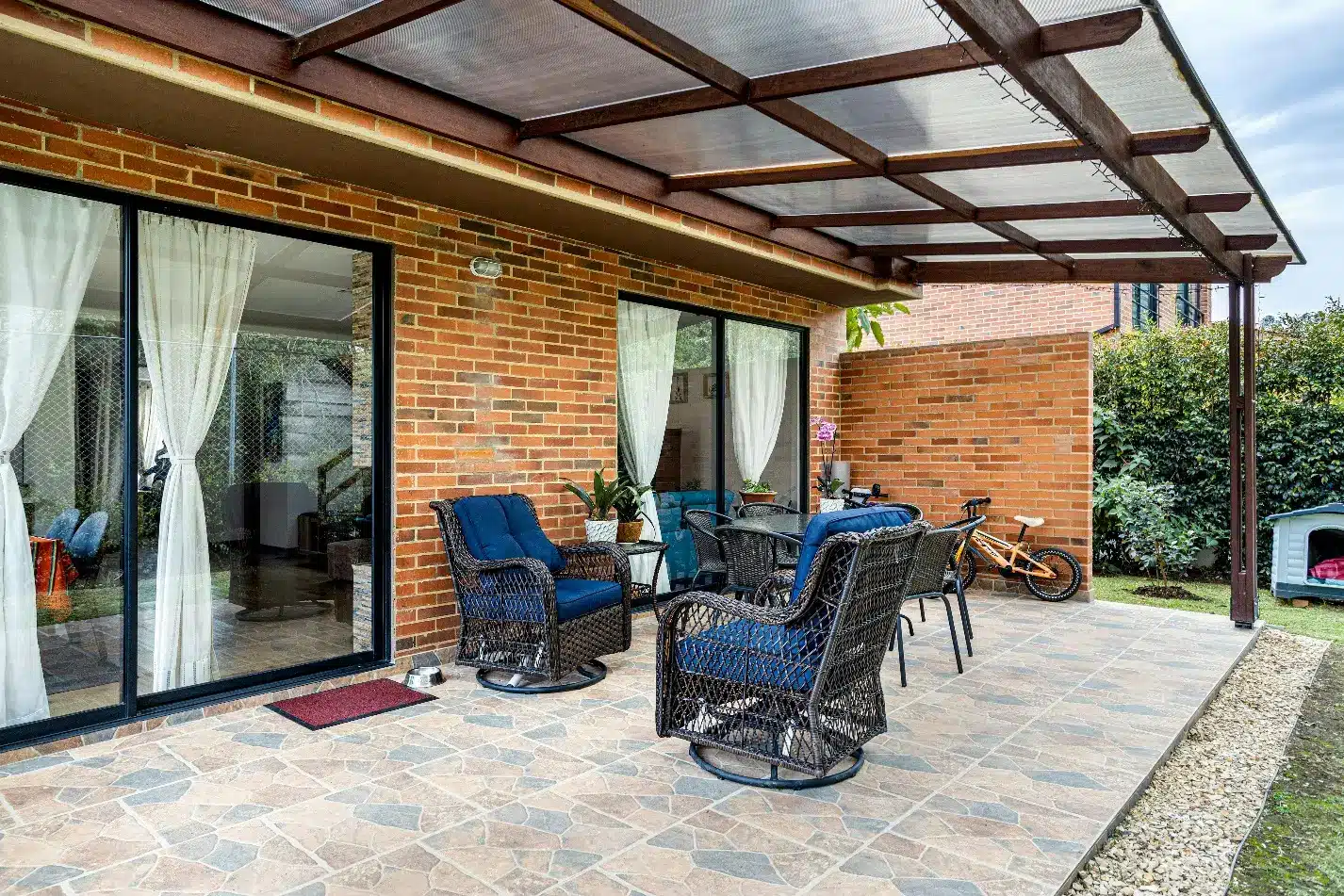 Covered patio with wicker chairs and table on tiled flooring near brick wall