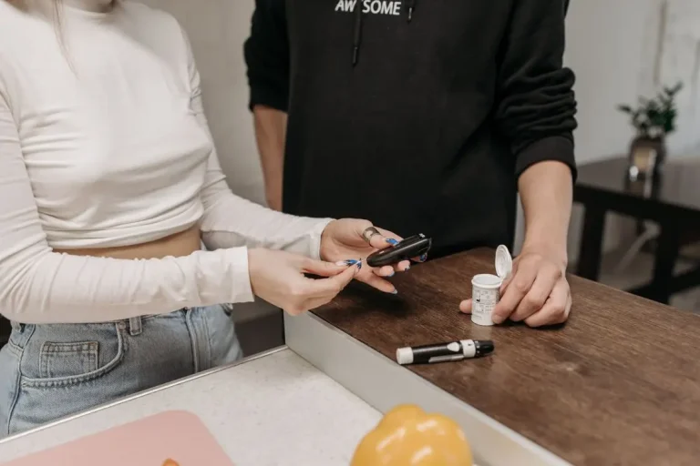 Two people checking blood sugar with glucometer at wooden counter in a kitchen setting