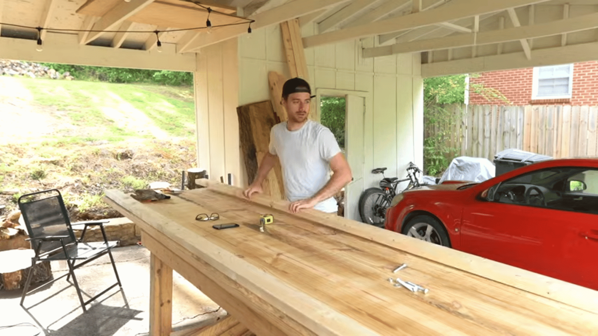 Man inspecting long wooden planks laid out on a garage workbench to plan a DIY farmhouse table.