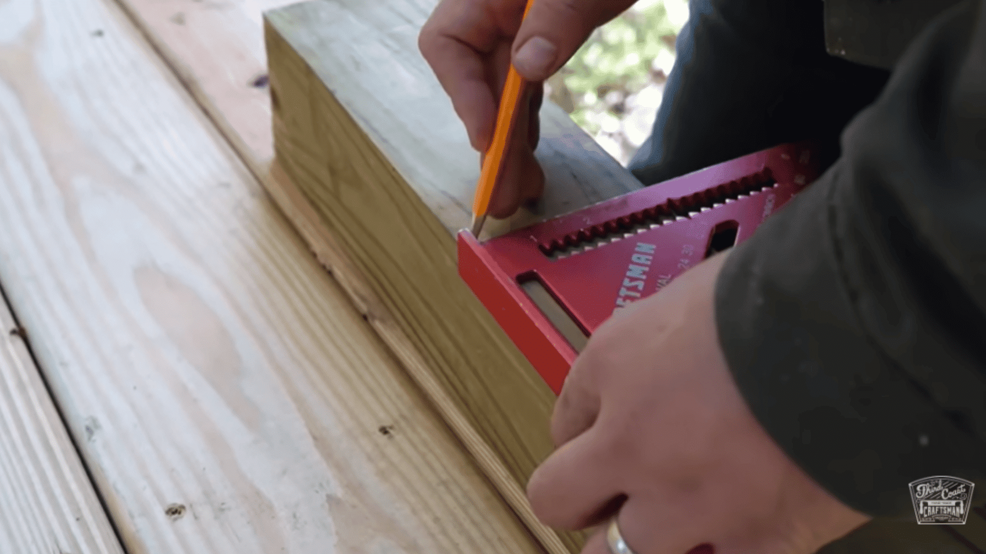 Marking a line on a wooden post with a pencil using a red speed square for deck railing placement