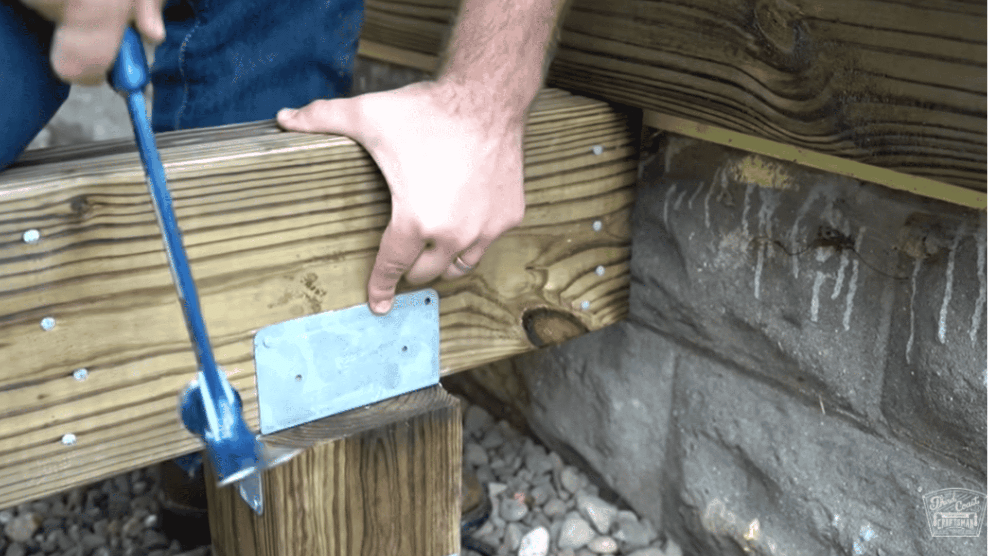Metal bracket securing a wooden beam to a post being hammered into place for a deck frame