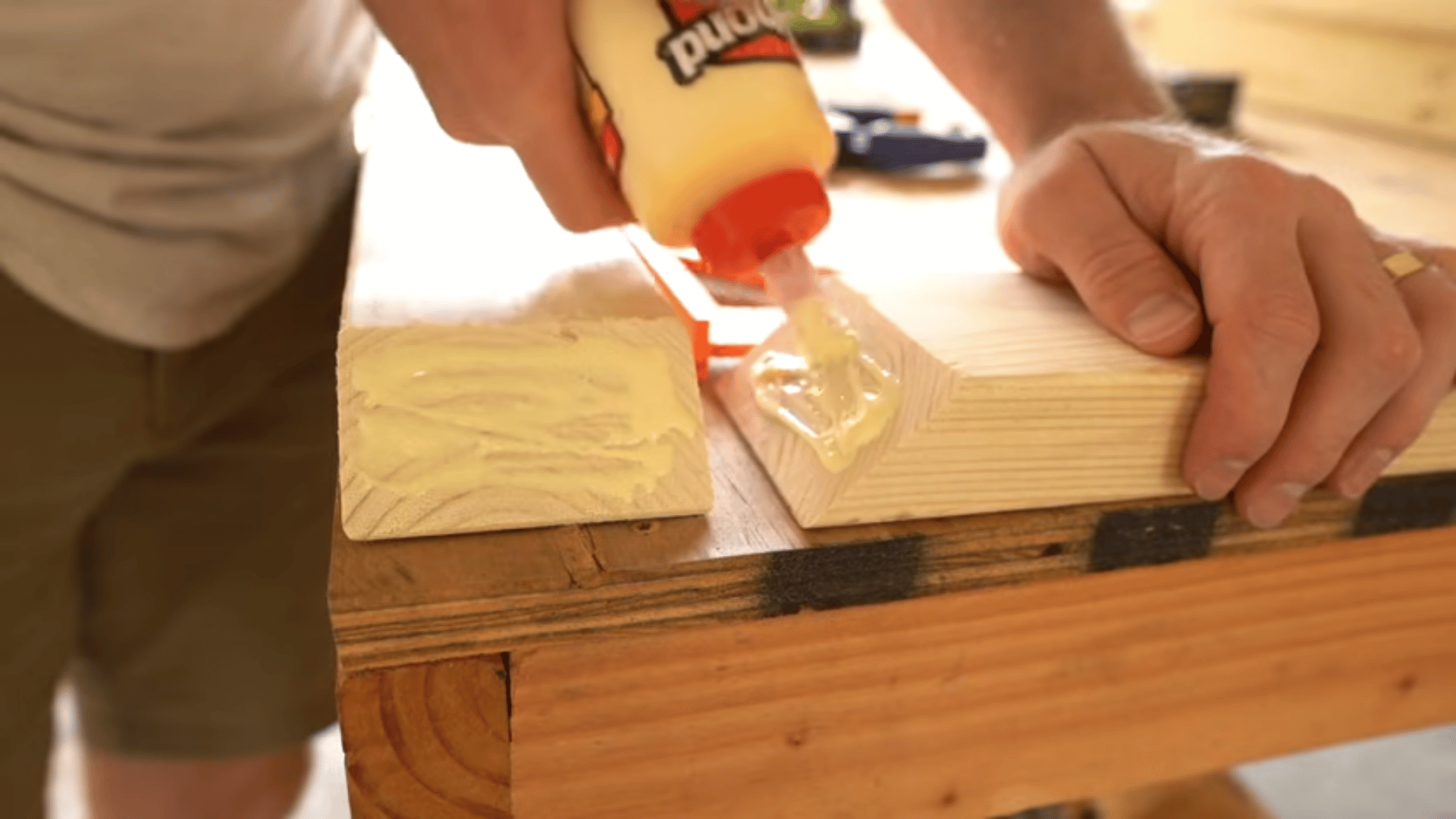 Person applying yellow wood glue from a squeeze bottle onto a mitered wood joint