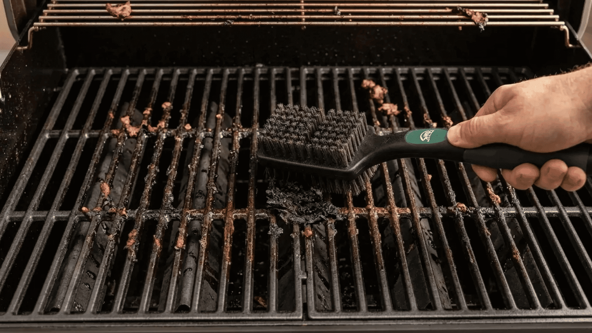 Person scrubbing greasy grill grates with a bristle-free grill brush during barbecue cleaning.
