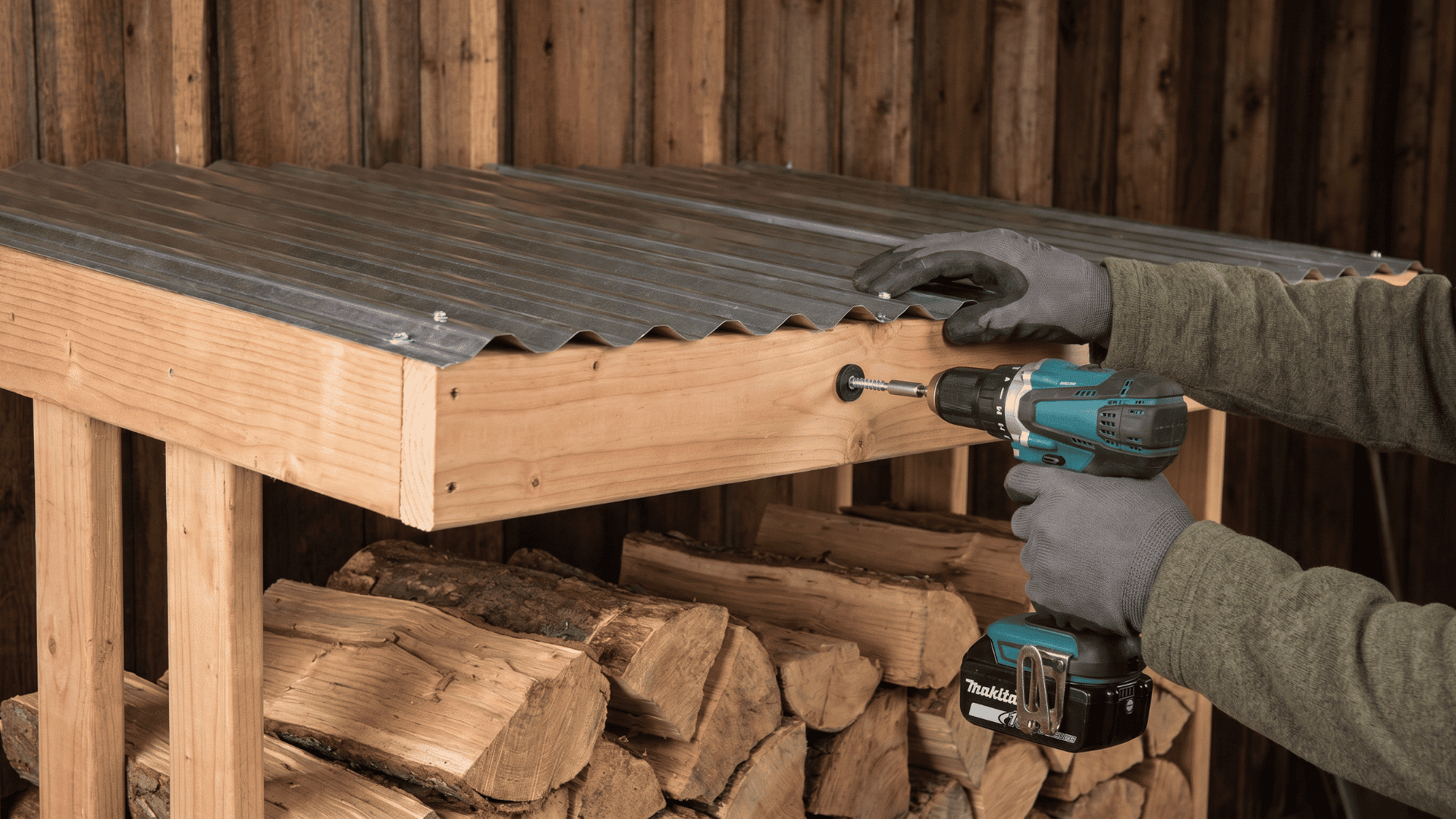 Person securing a sloped roof on a wooden firewood rack with screws and rubber gaskets