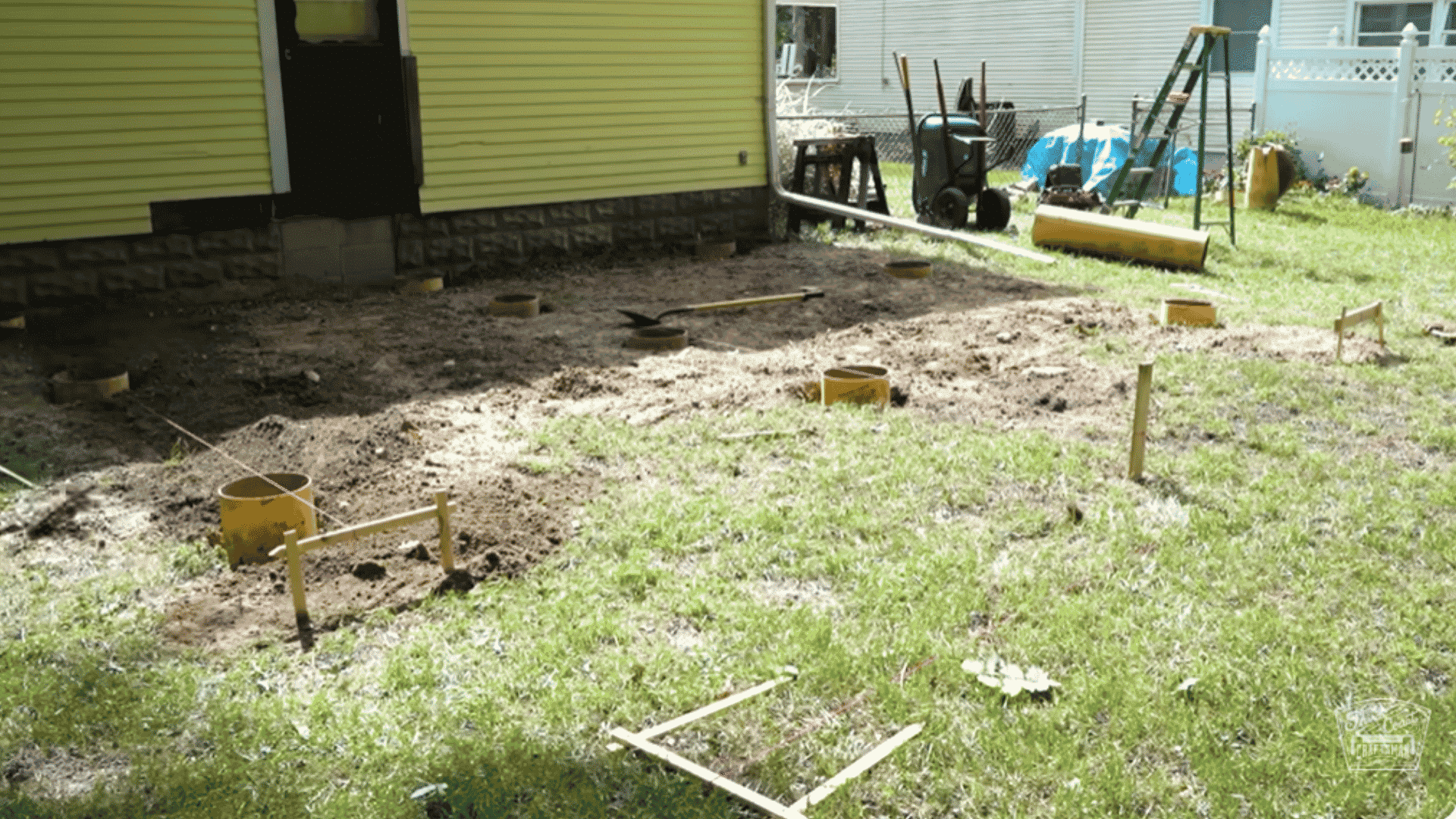 Post holes with yellow concrete forms set in the ground and tools around the area for building a deck