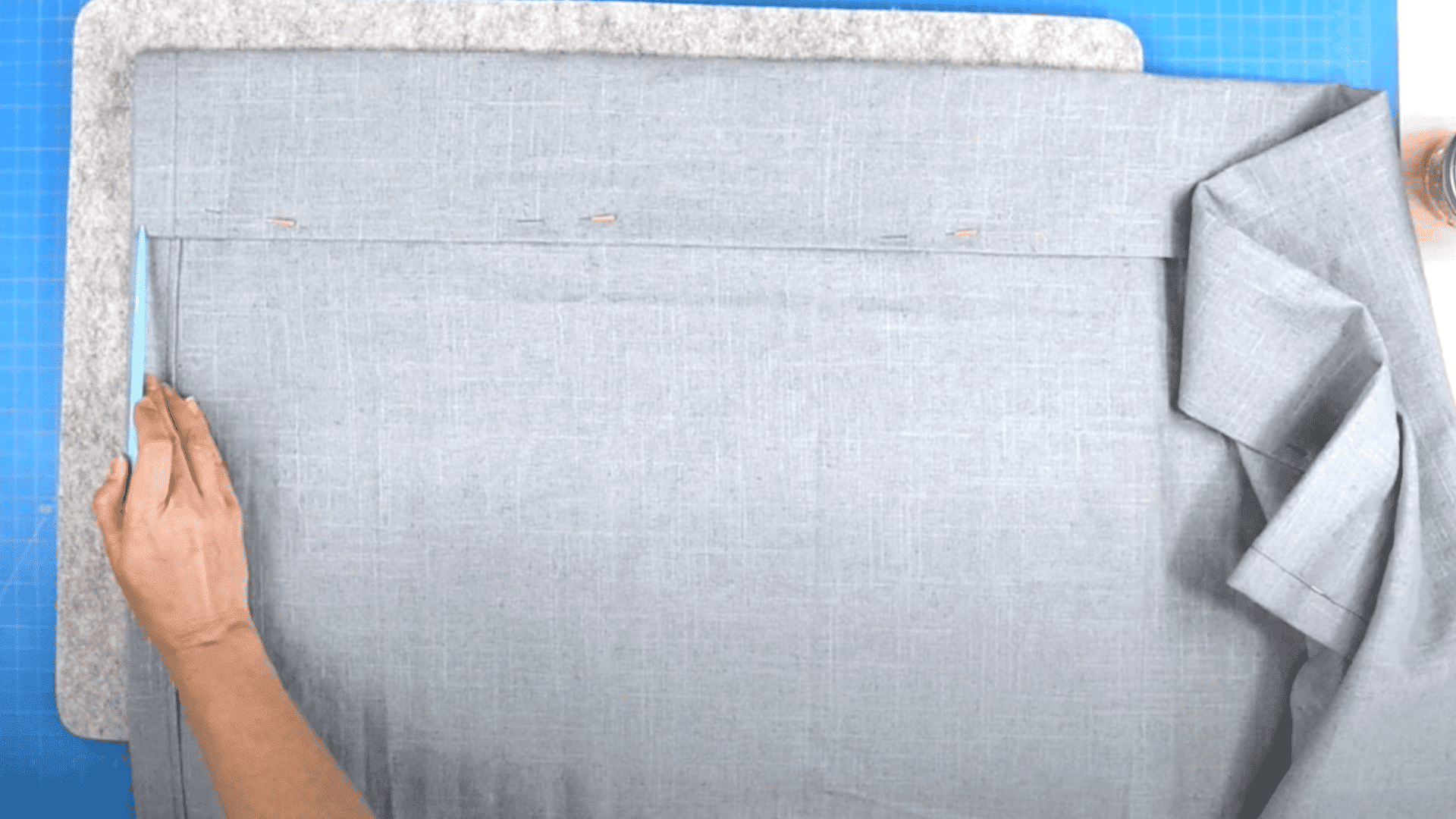 A person's hand using blue tailor's chalk to mark a straight line on folded grey fabric over a blue mat.