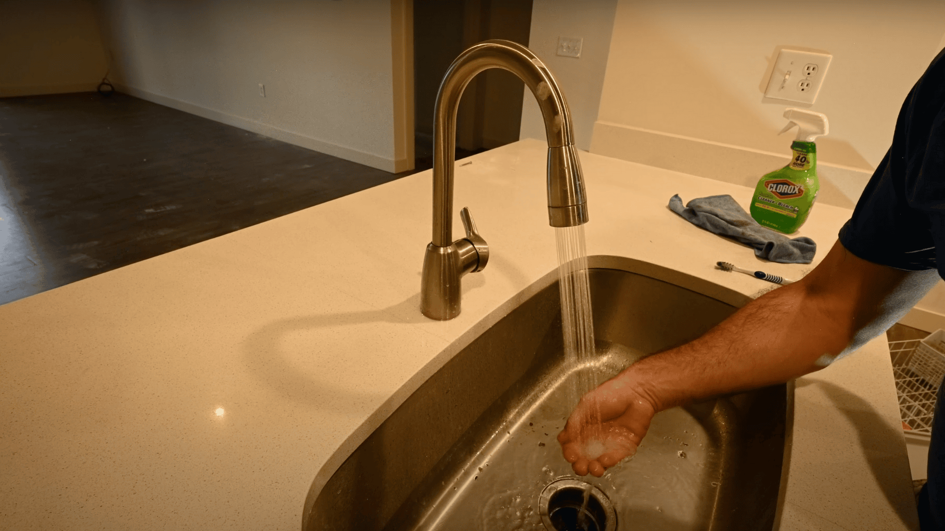 An image of a person checking the water temperature at a kitchen sink by running hot water over their hand from a sleek, curved faucet.