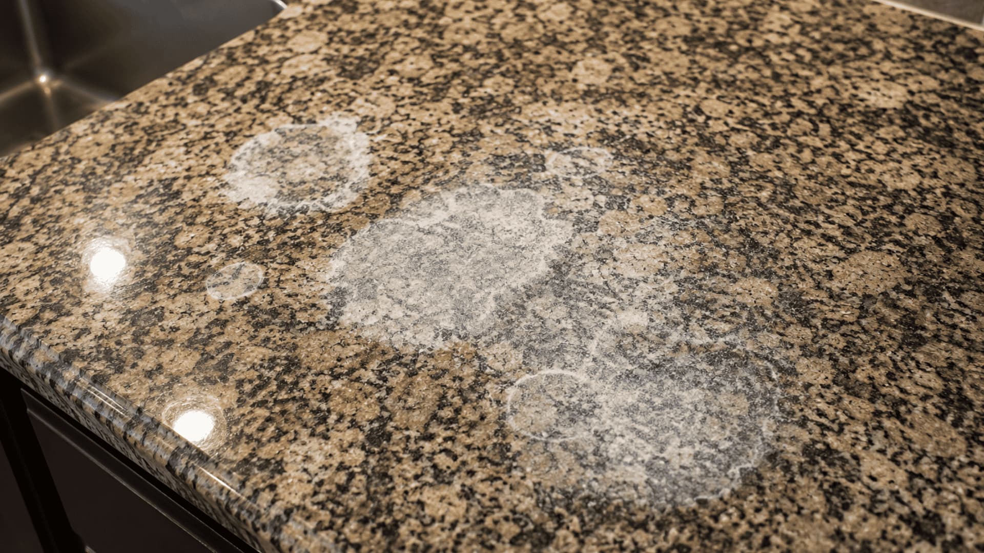 Damaged granite countertop showing dull, cloudy white etch marks caused by acidic vinegar exposure.