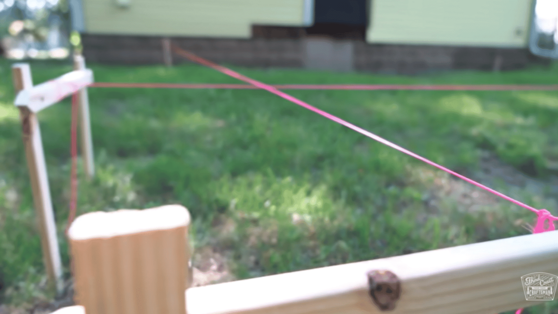 Stakes and red string lines marking the corners and boundaries of a deck on a grassy yard