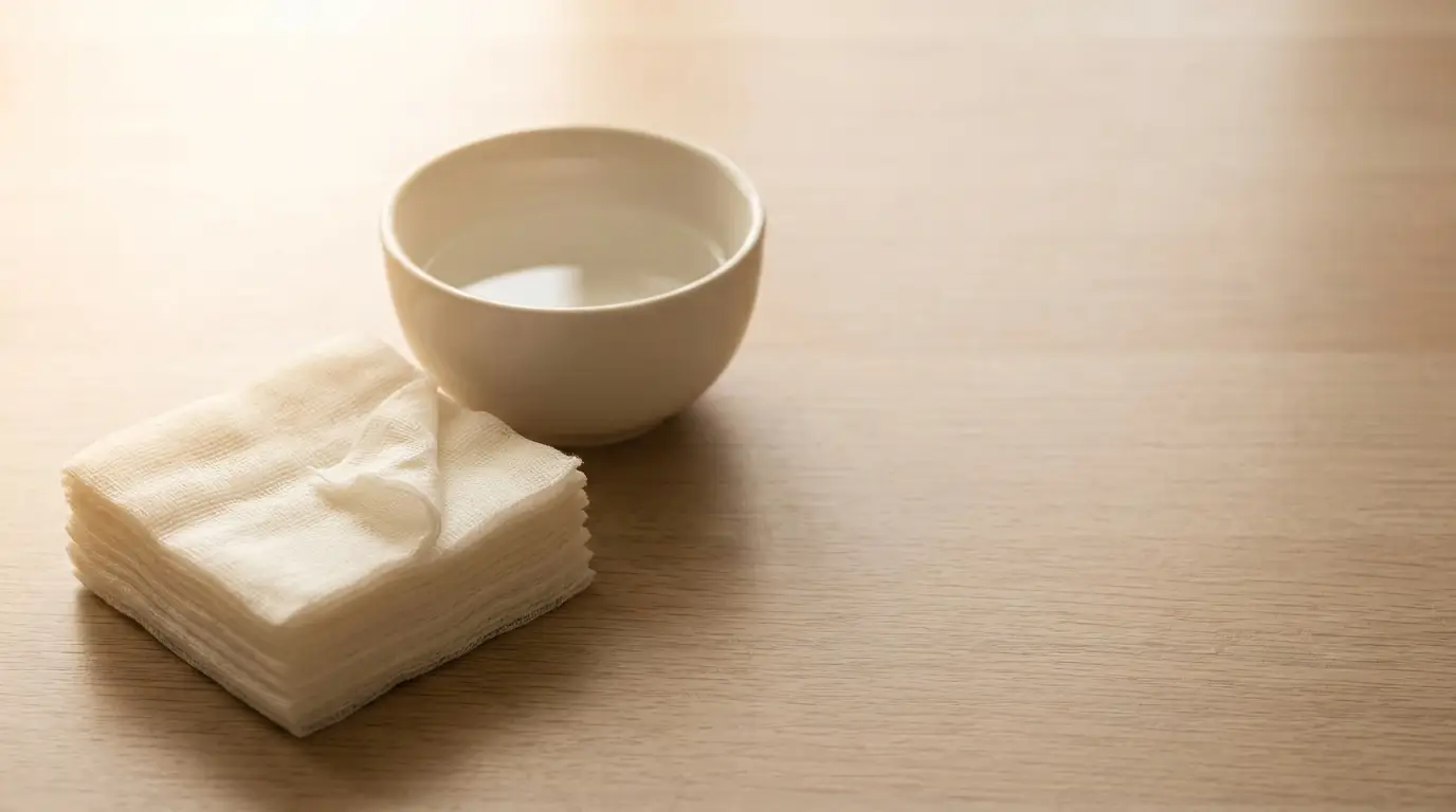 Stack of gauze pads beside a white bowl on a wooden table