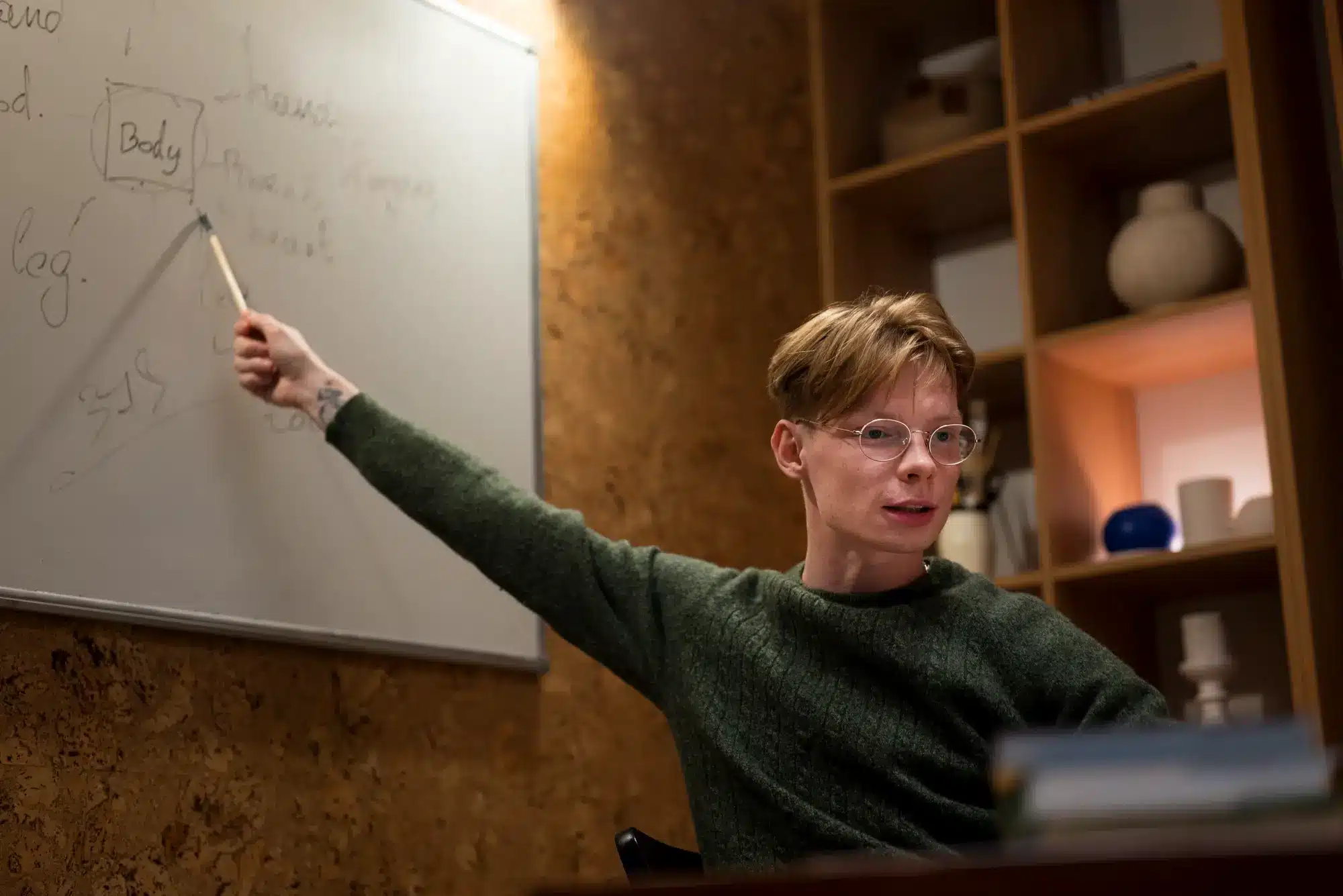 Person in green sweater pointing at notes on whiteboard in cozy office setting