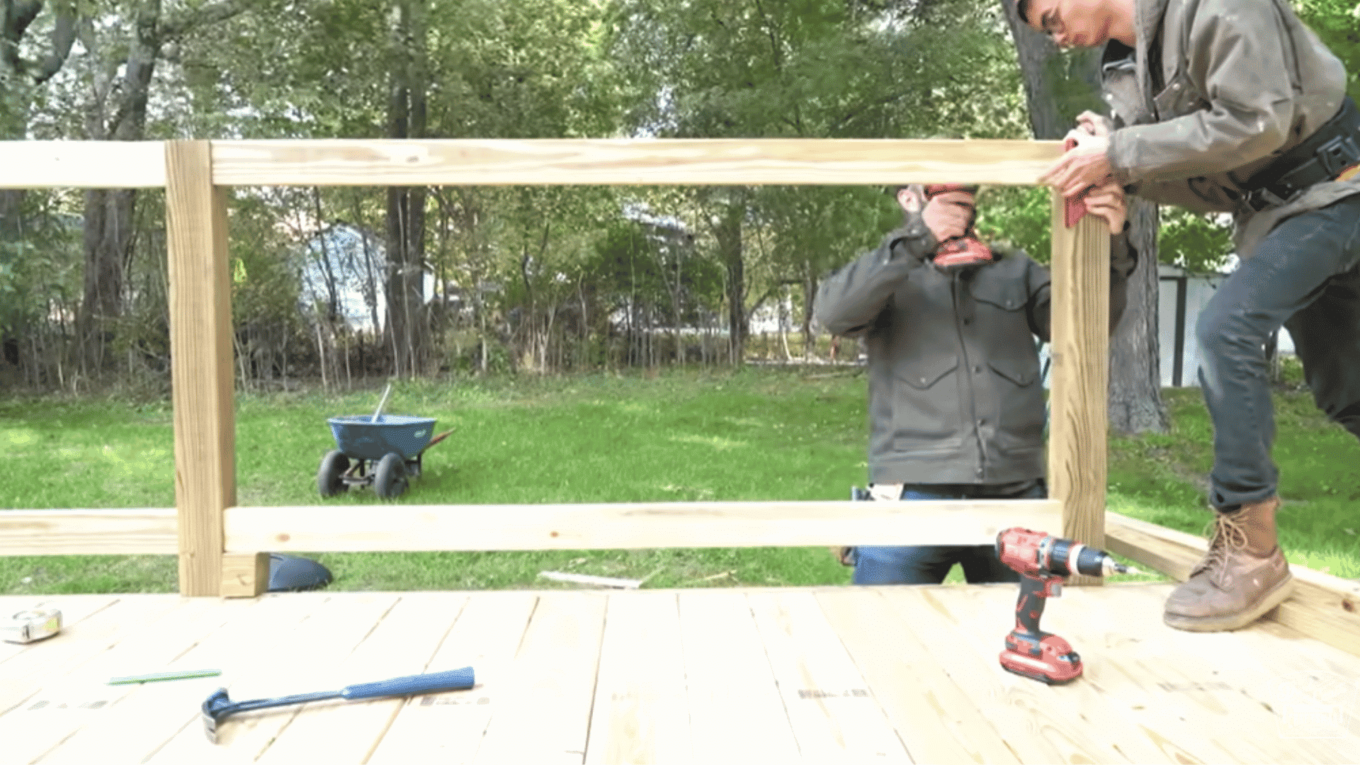 Top and bottom rails being attached to vertical posts on a wooden deck railing with two people working