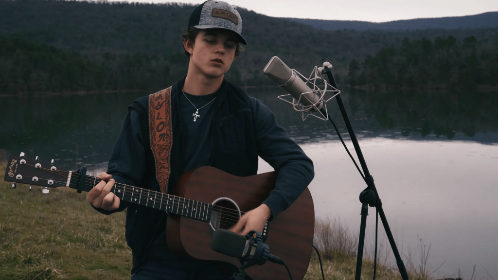 Musician Waylon Wyatt performing outdoors with an acoustic guitar, representing his raw country music style.