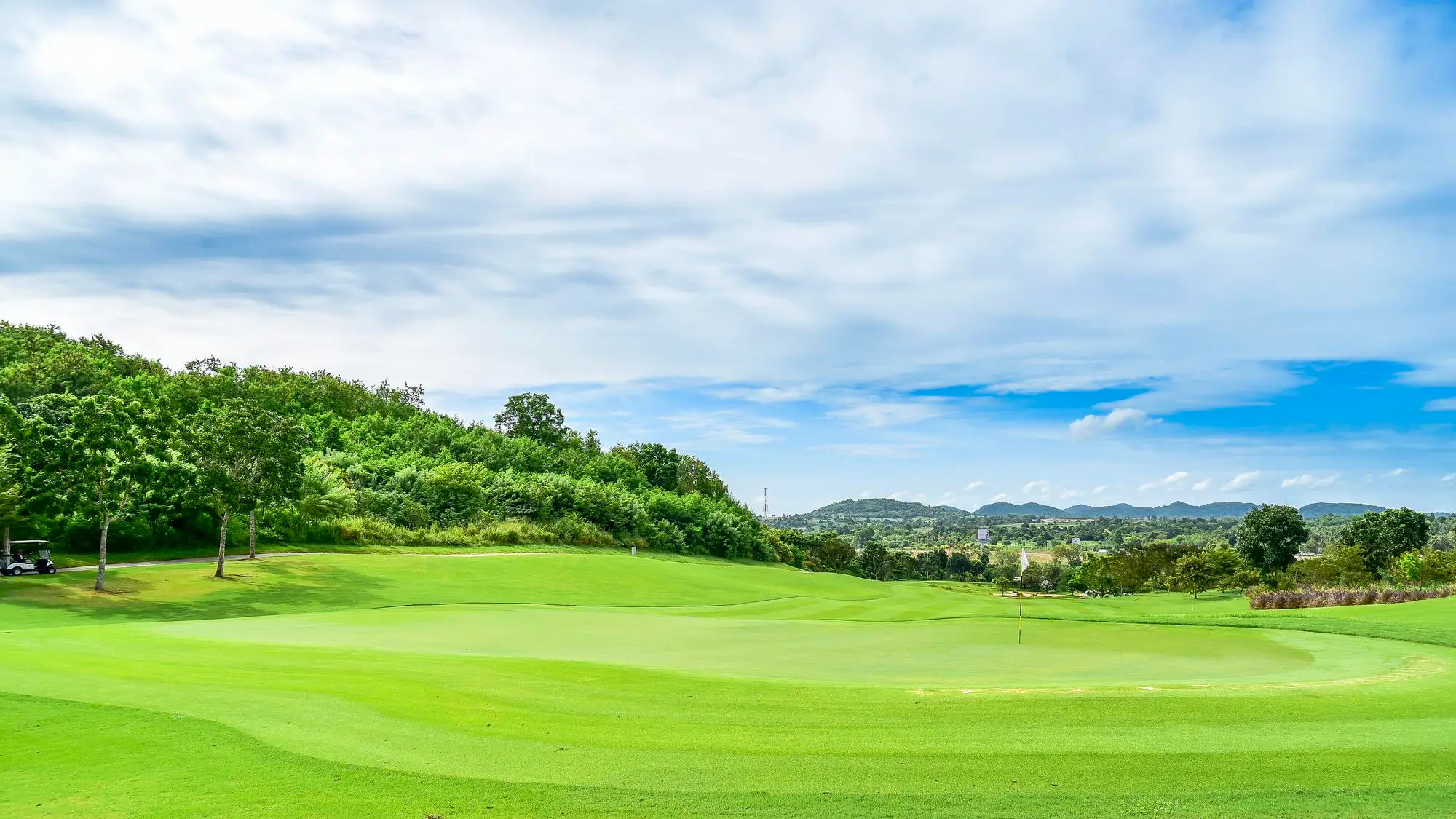 Green golf course under blue sky with hills and trees in the distance