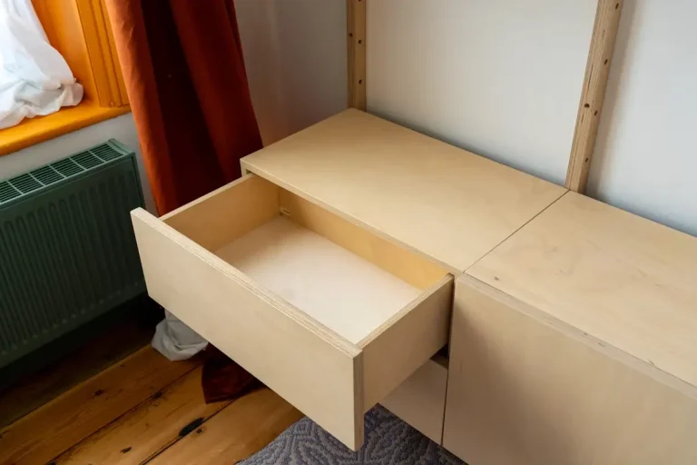 Open wooden drawer in modern cabinet beside window with orange curtain and green radiator