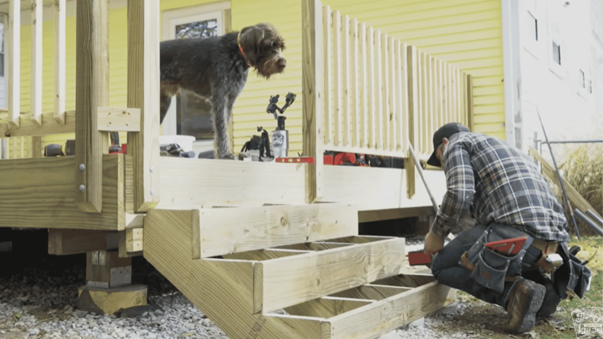 Wooden stair stringers being installed with a person working next to a deck and a dog standing on the deck