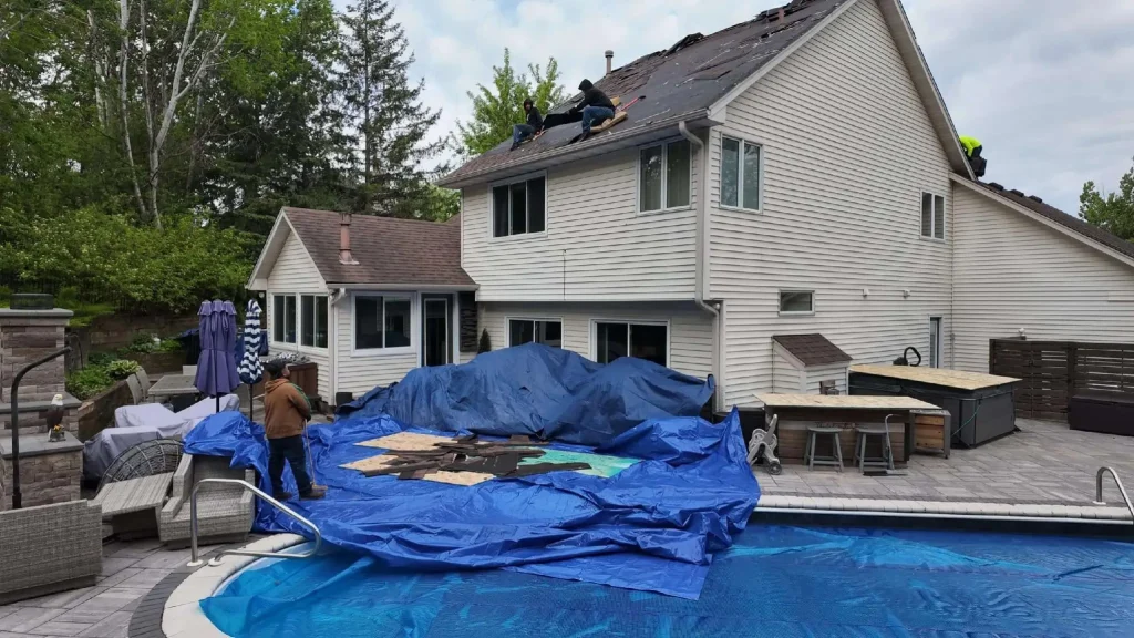 Workers repairing house roof with blue tarps spread on ground in backyard beside pool