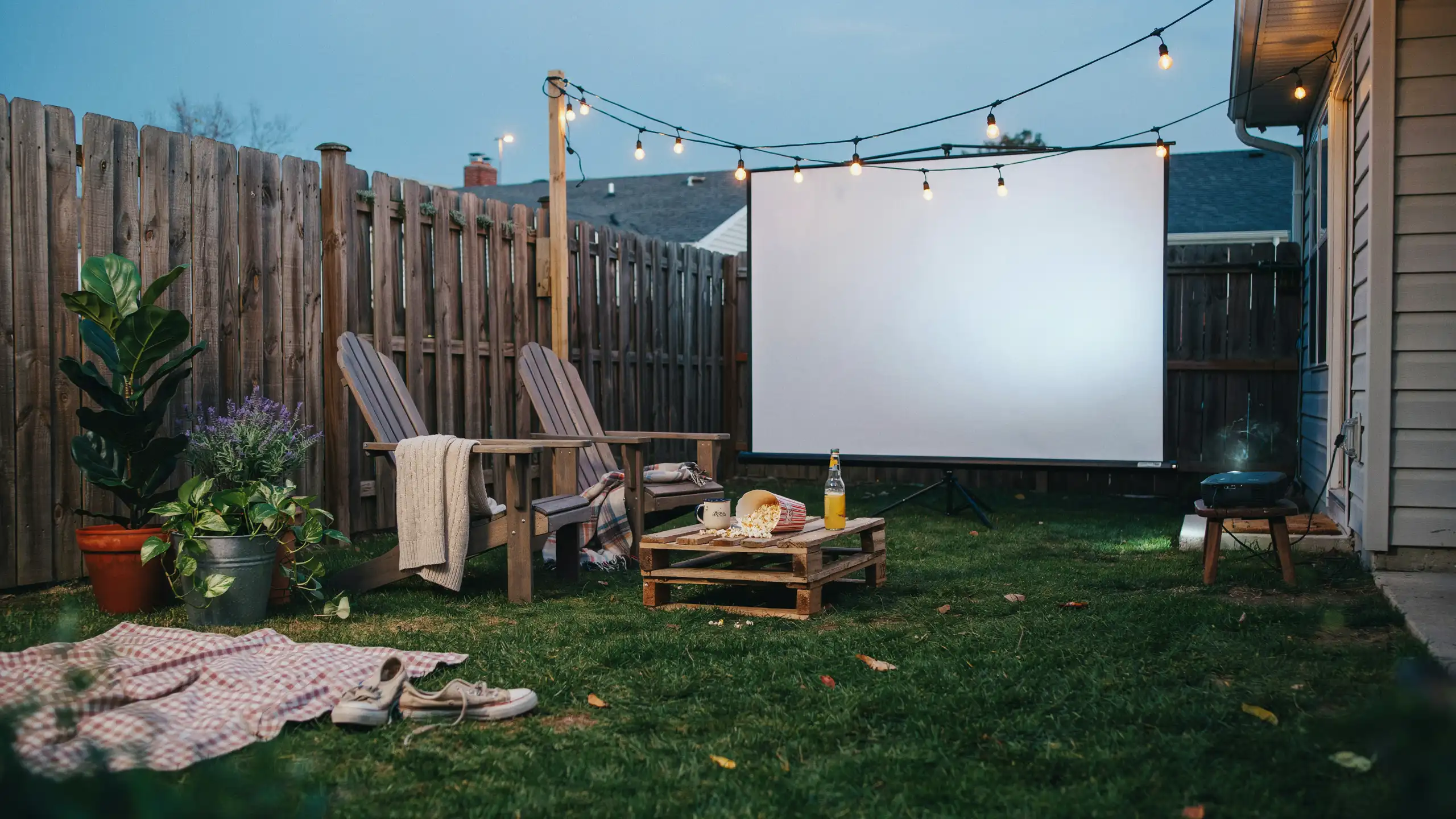 Backyard movie setup with outdoor screen, projector, seating, and string lights.