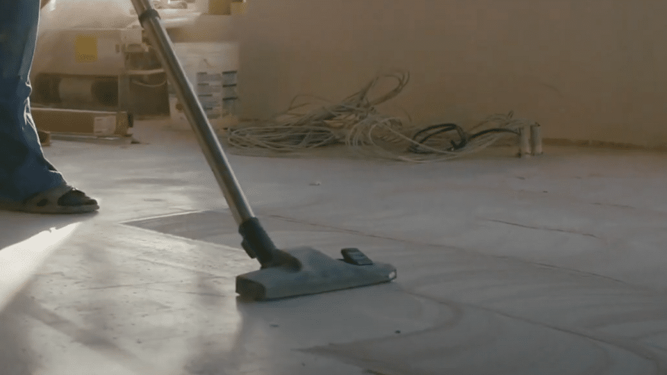 A person using a specialized extraction nozzle to vacuum soapy liquid and clean a grey outdoor carpet surface.
