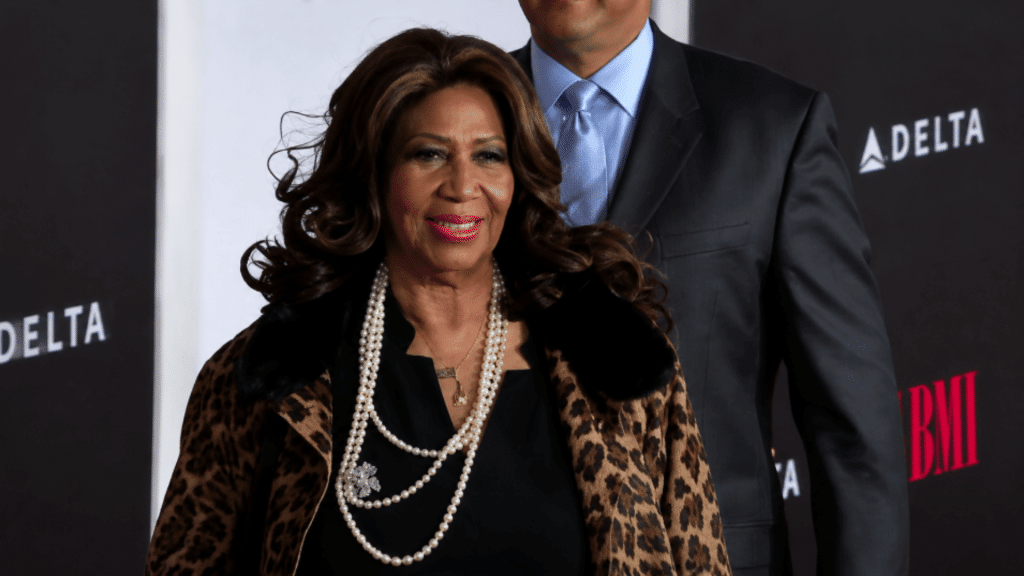 Aretha Franklin at an event wearing a black outfit with pearl necklaces and a leopard-print coat.