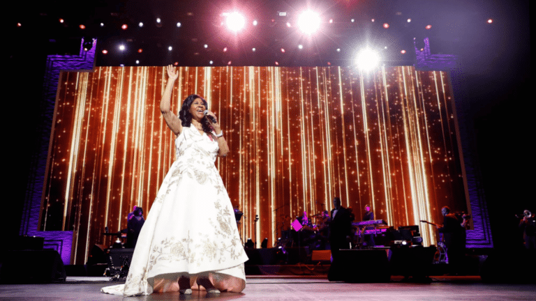 Aretha Franklin performing live on stage in a white gown during a music concert.