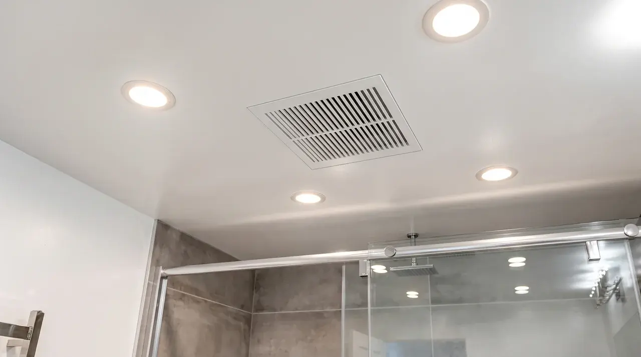 Bathroom ceiling exhaust fan with a clean vent cover installed above modern tiled surroundings.