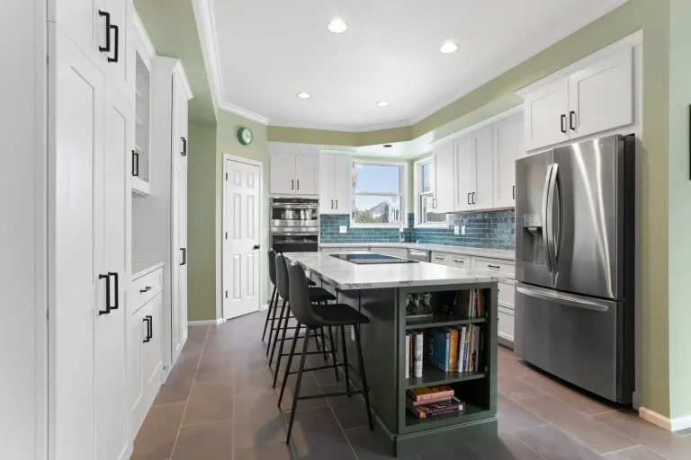 Modern kitchen with white cabinets, stainless steel refrigerator, and island with bar stools and cookbooks