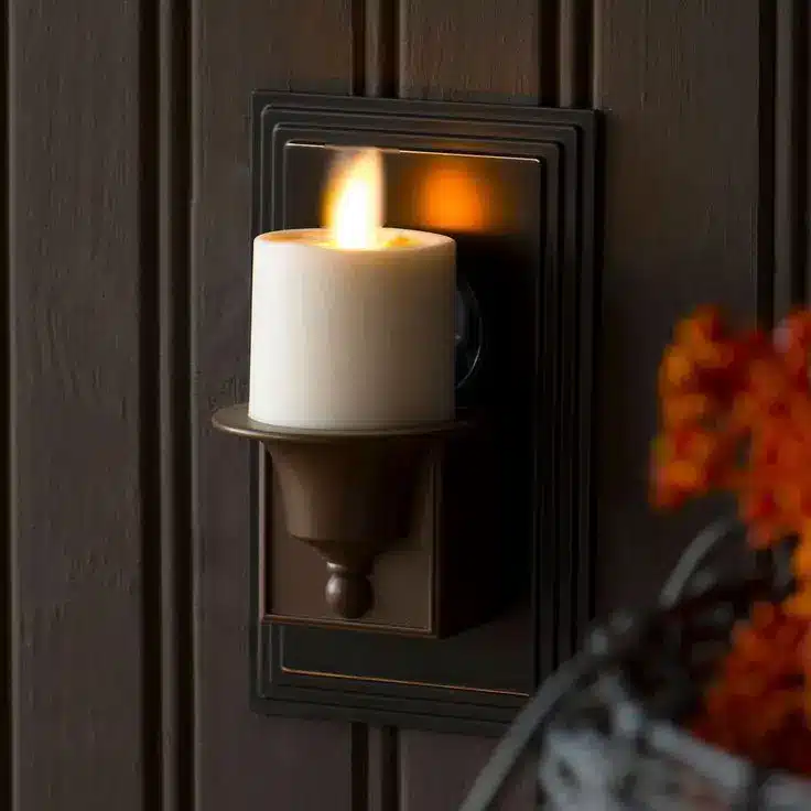 Bronze candle sconce with lit pillar candle on wooden paneled wall