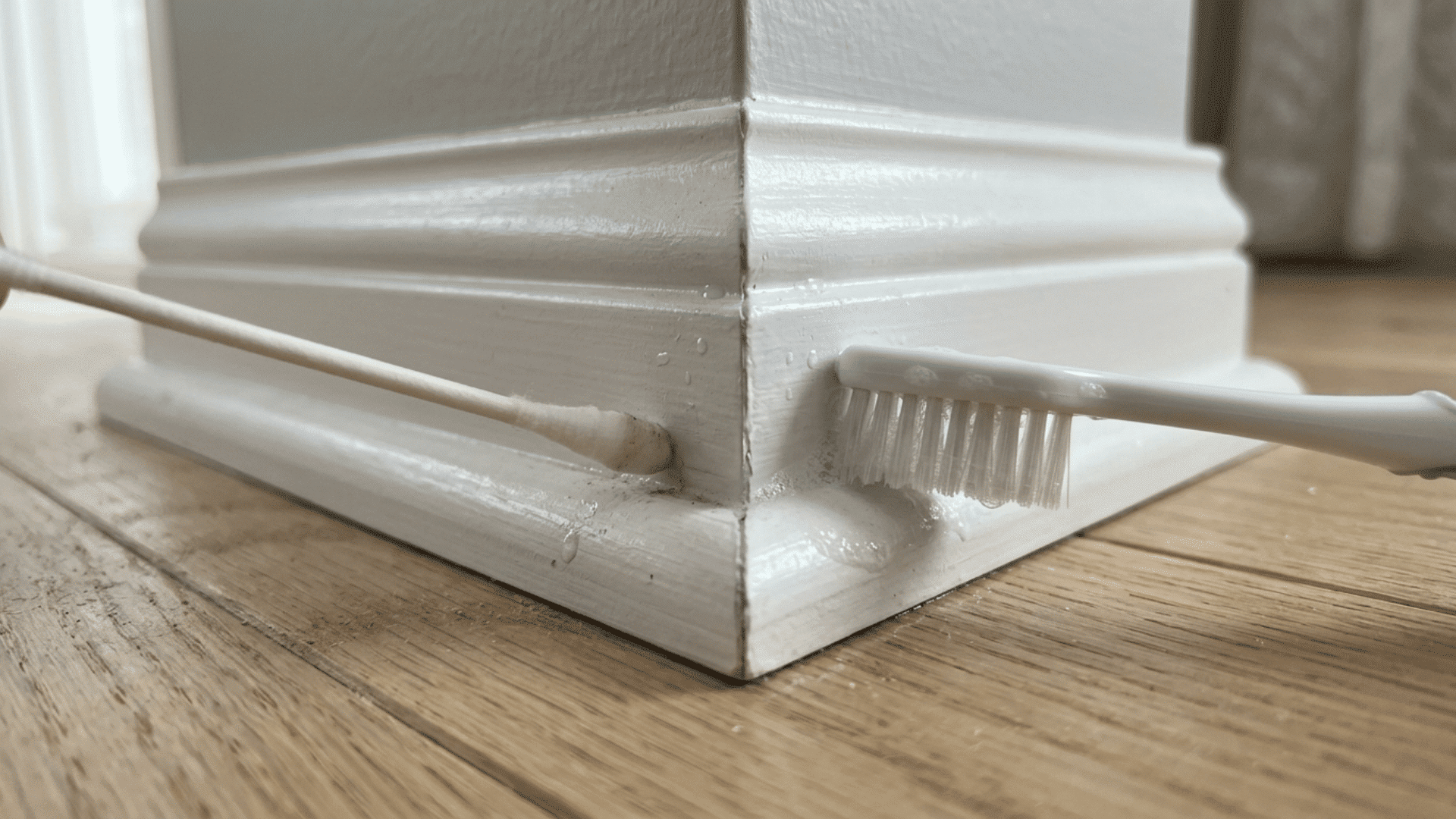 Cotton swab and toothbrush cleaning baseboard corner grooves and seams
