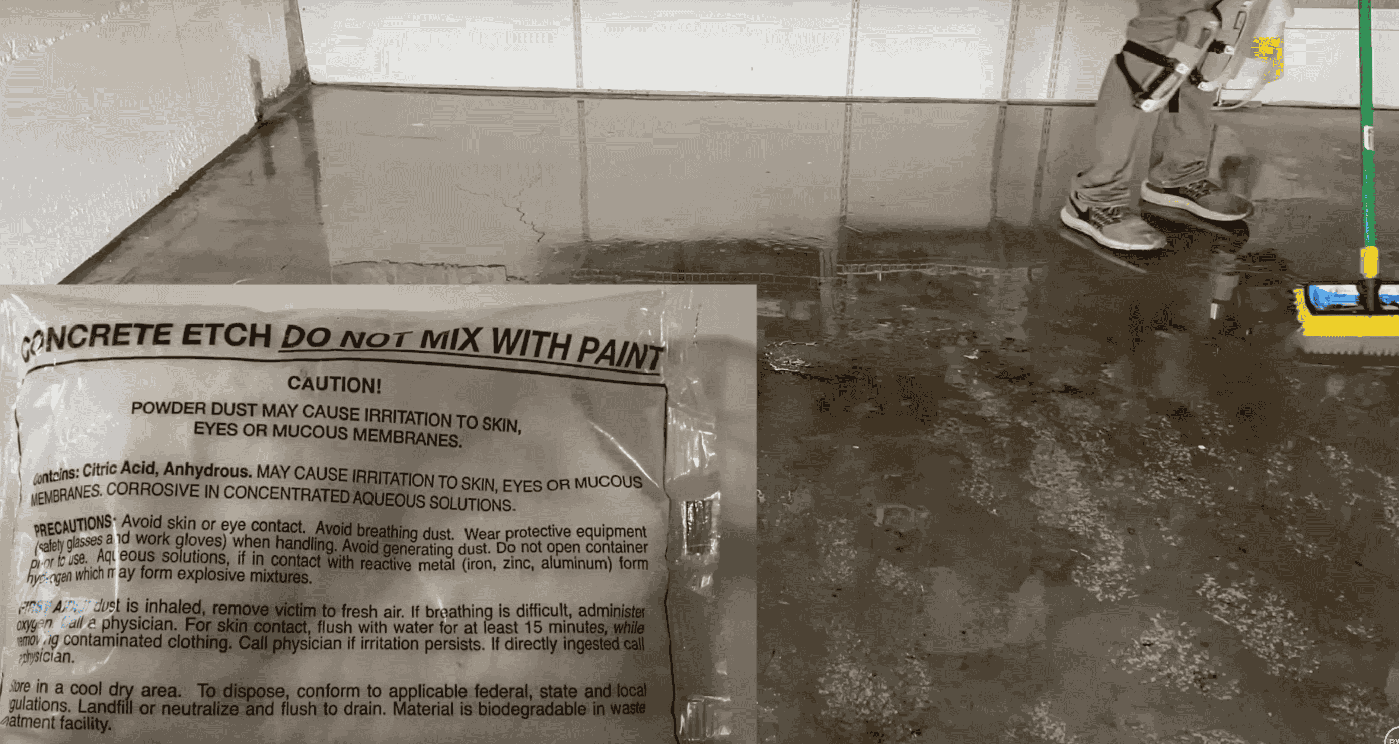 A bag of concrete etching powder sits on a wet garage floor while a person prepares to scrub the surface.