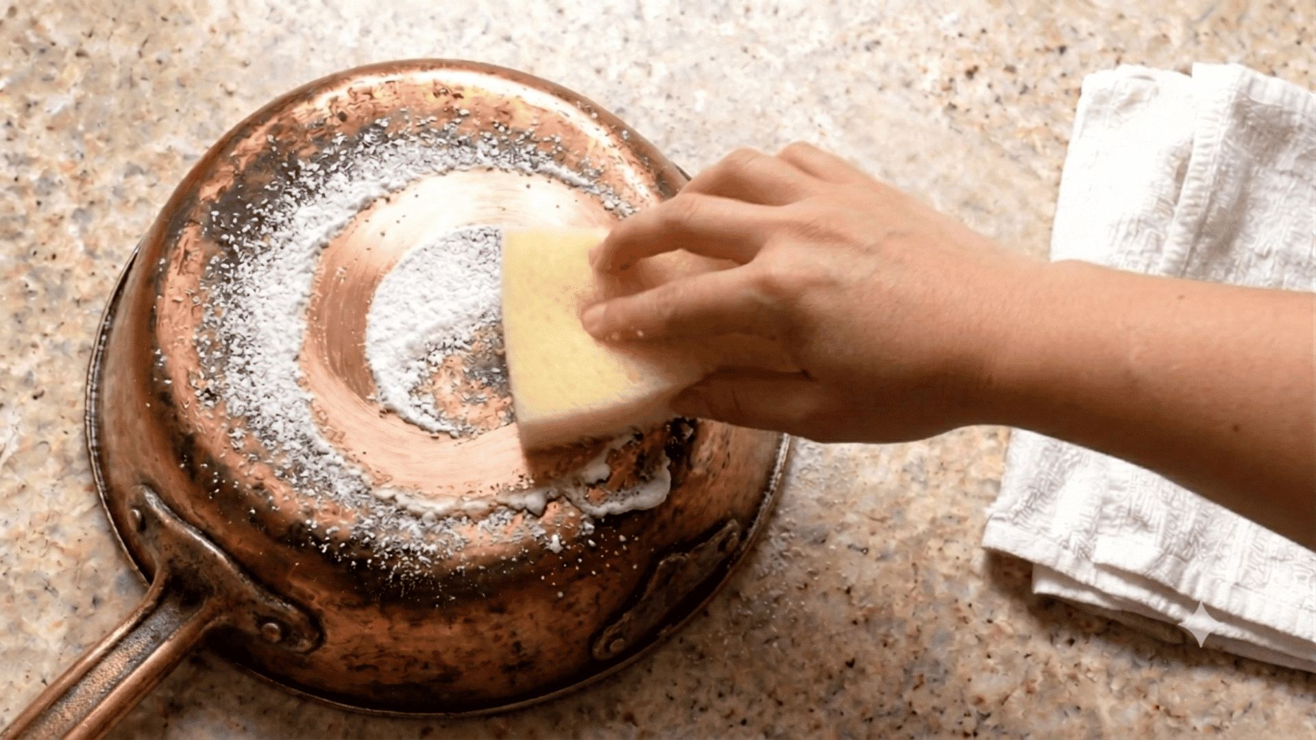 Hand cleaning a copper pan with salt on a kitchen countertop
