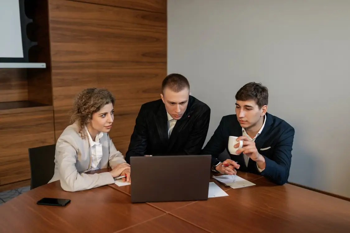 Three professionals discussing work around laptop in modern conference room