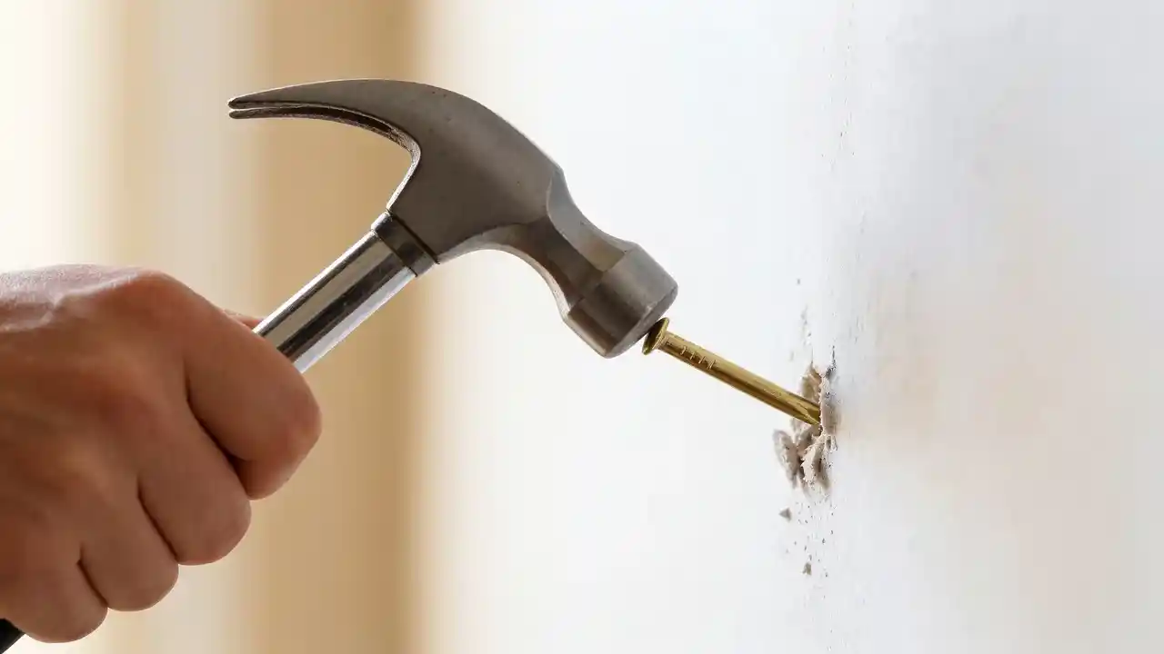 Picture nail driven at 45-degree angle into white wall demonstrating correct technique to hang pictures on wall.