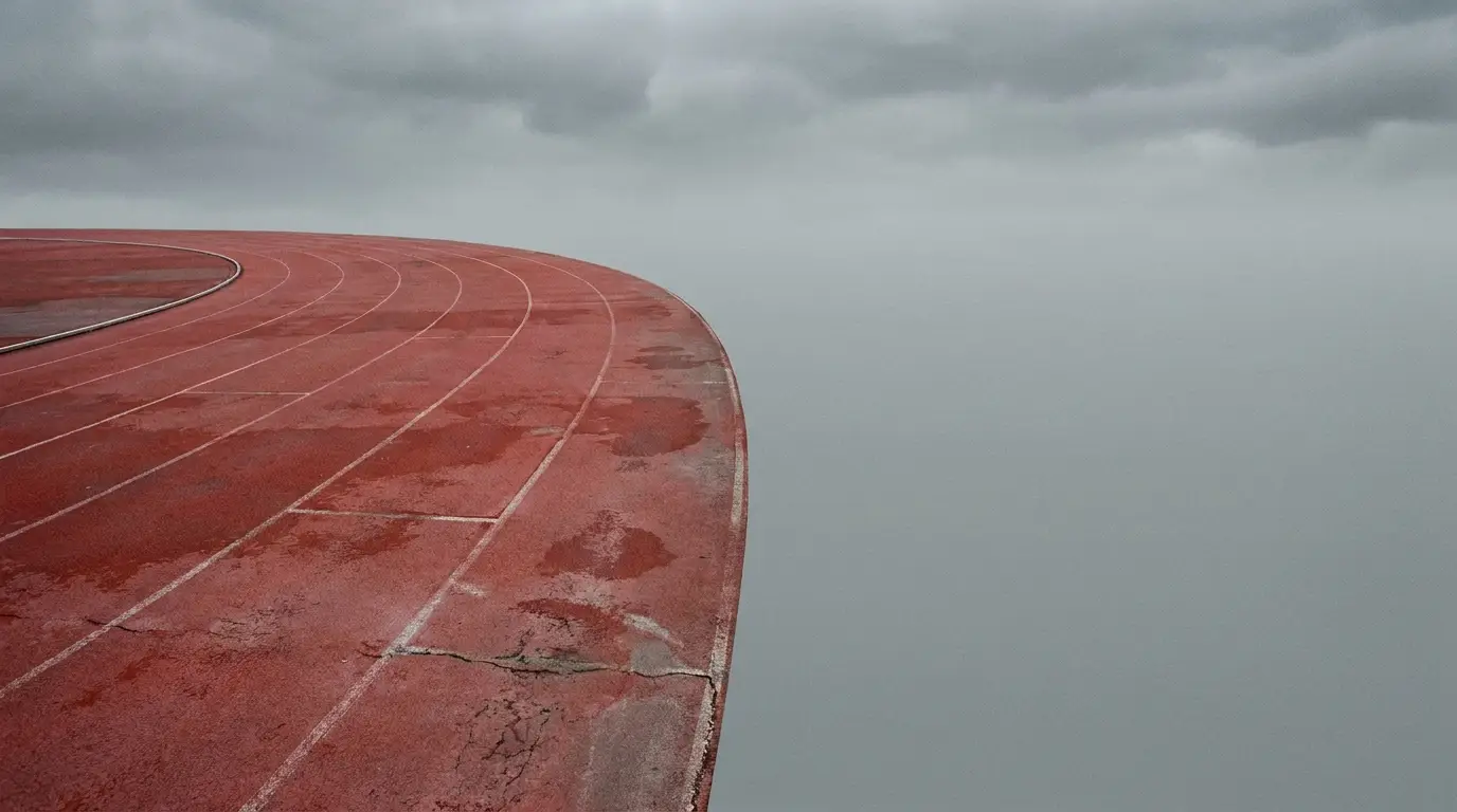 Curved red running track under overcast sky with visible cracks and wear