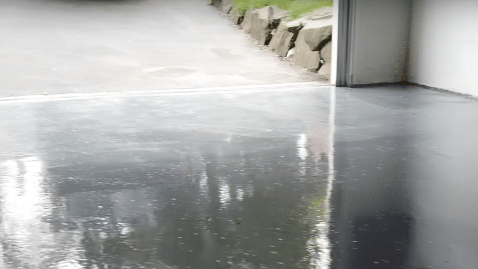A highly glossy, freshly finished grey epoxy garage floor reflecting light from an open garage door during the curing process.