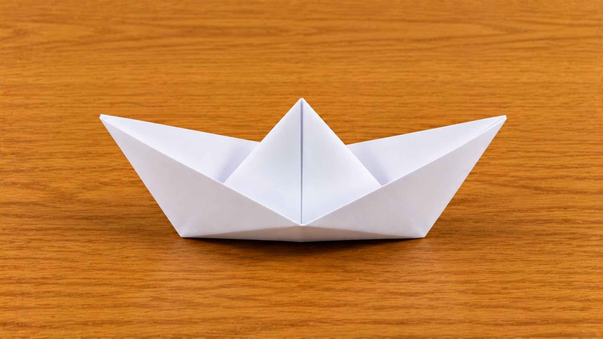 White origami paper boat resting on a wooden table with soft natural lighting and subtle shadows.