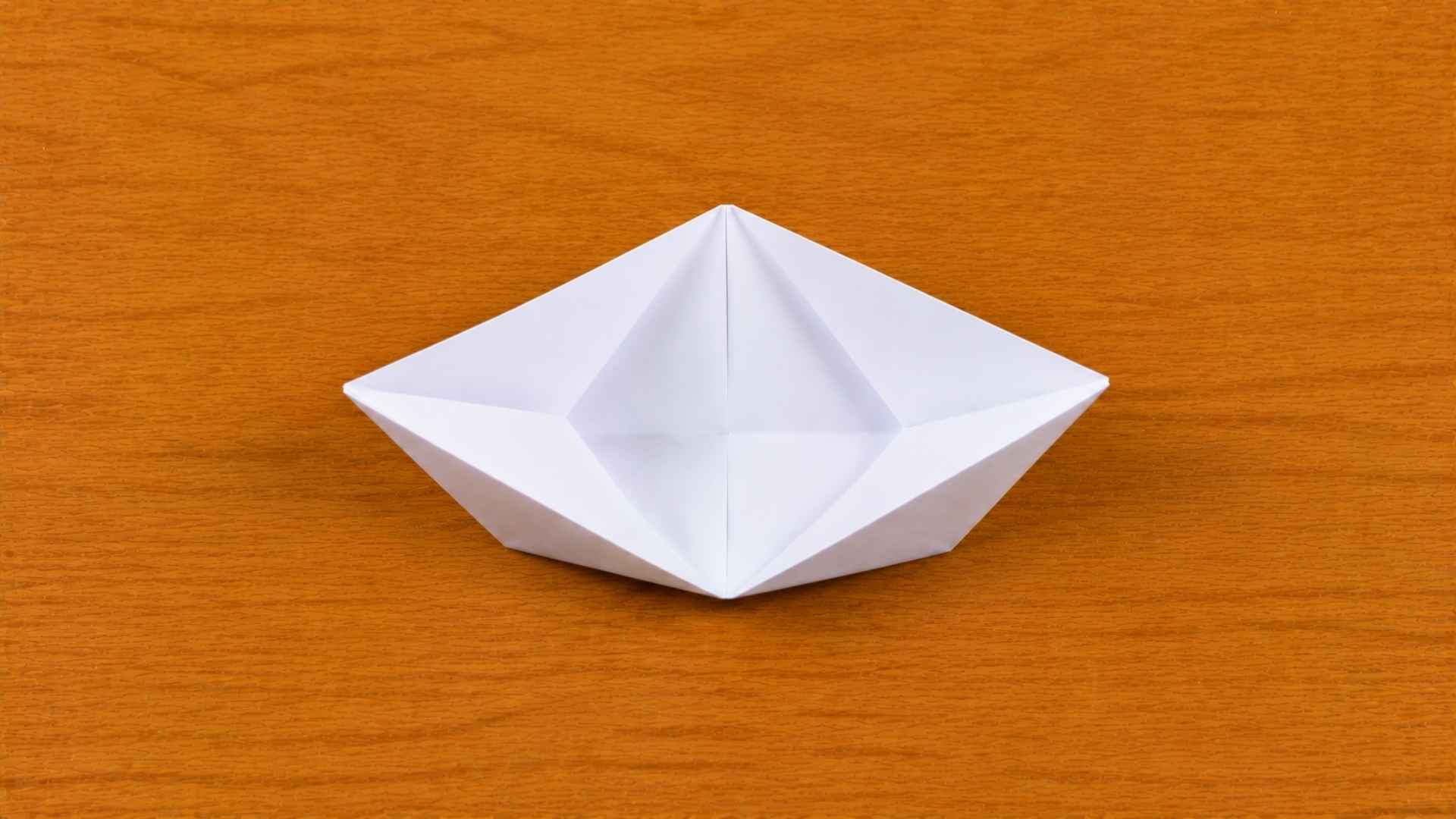 White origami paper partially opened into a boat shape resting on a wooden table with soft natural lighting.