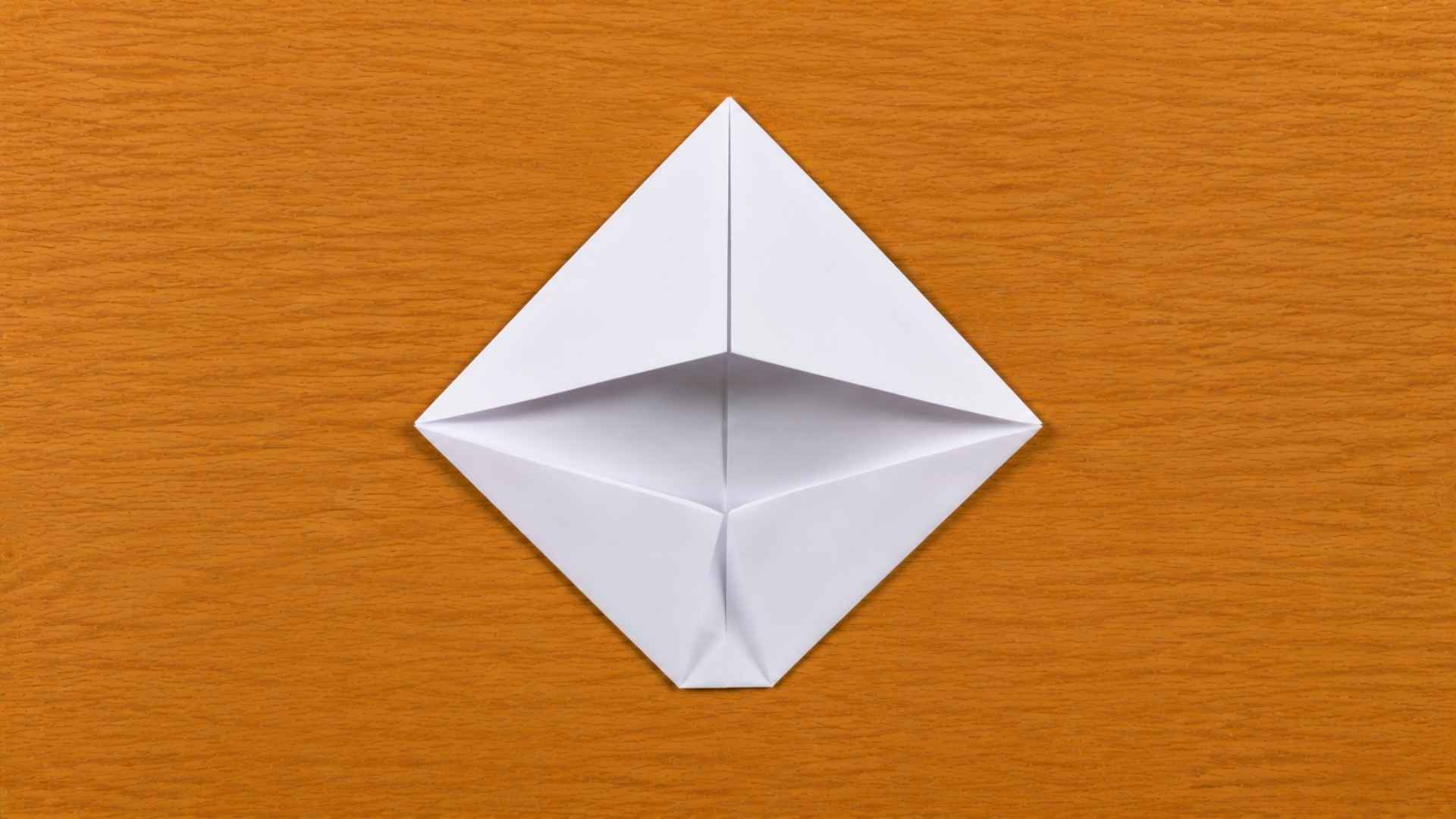 White origami paper folded into a square pocket shape resting on a warm wooden table with soft natural lighting.