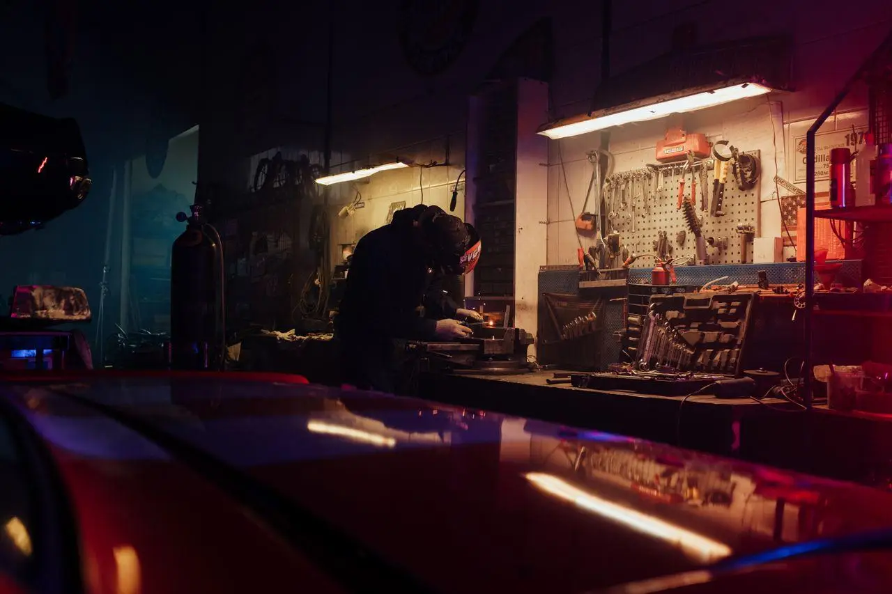 Mechanic in dimly lit garage working on car engine with tools on wall and workbench