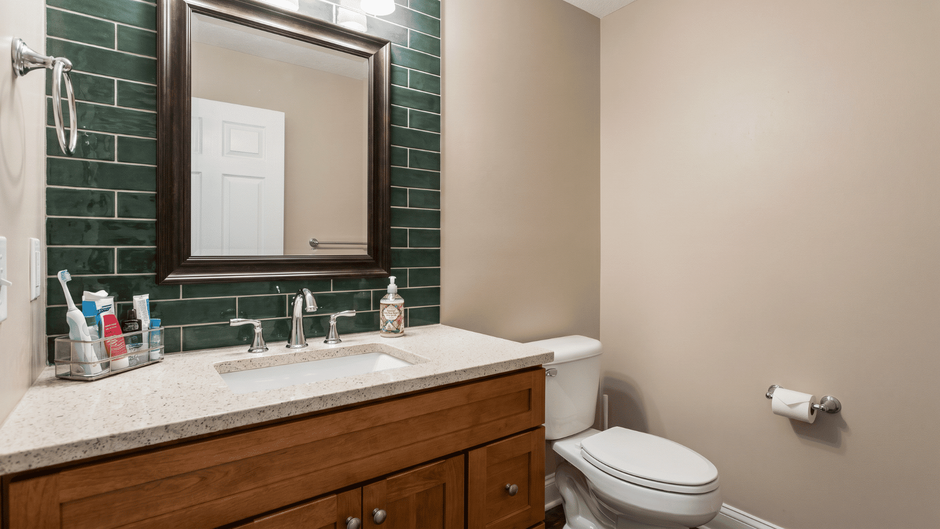 Bathroom vanity with dark green tile backsplash, mirror, sink, and white toilet.