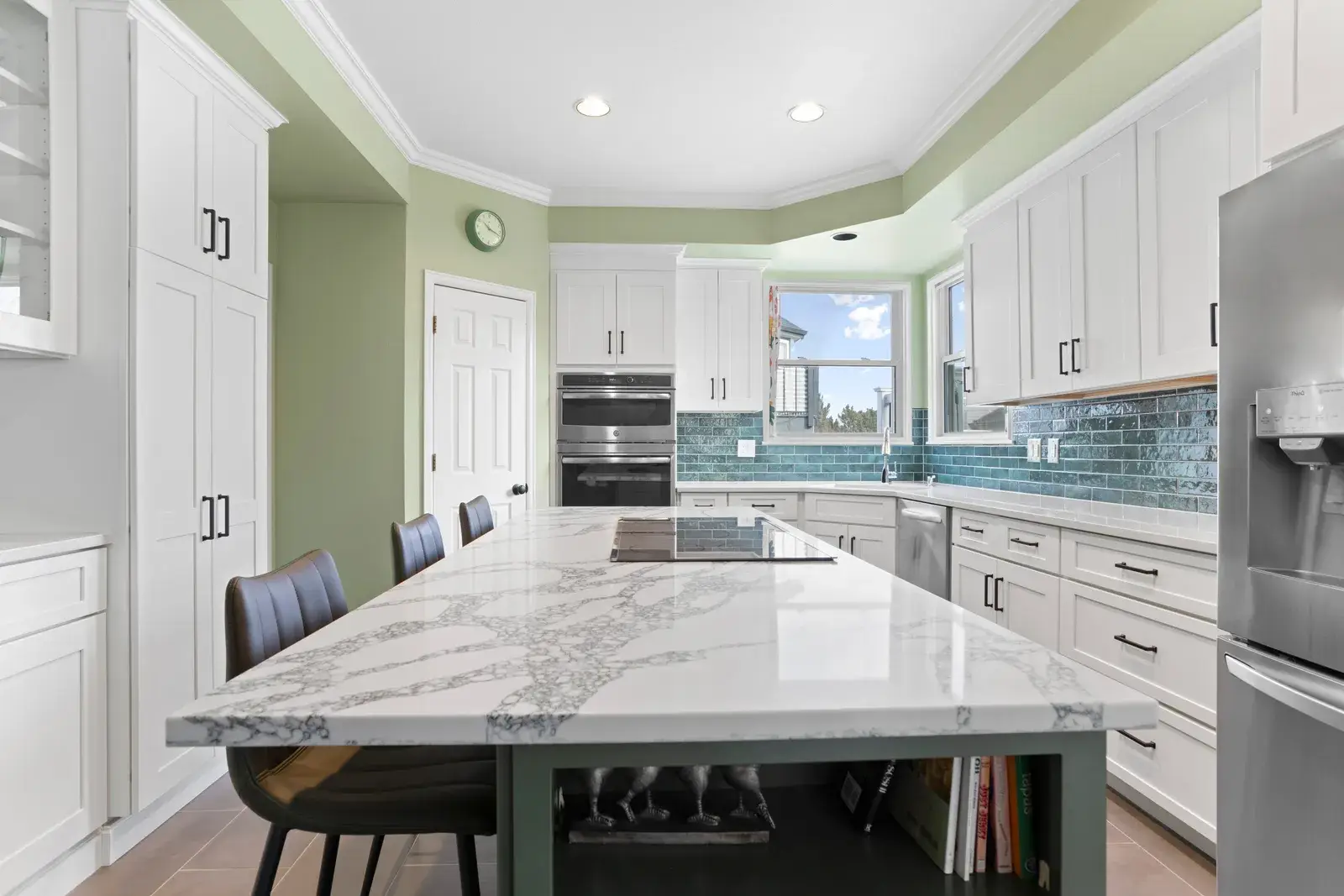 Modern kitchen with marble-topped island and green walls, featuring white cabinetry and stainless steel appliances