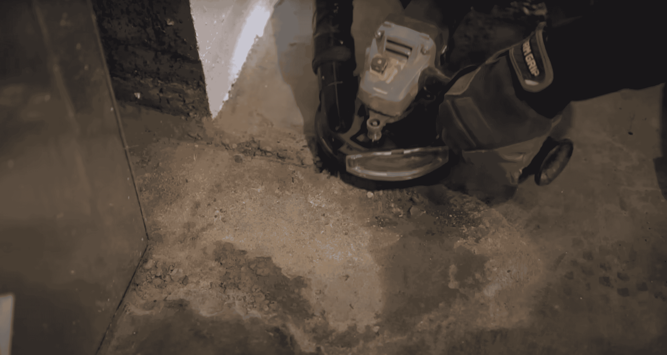 A person using an angle grinder to clean out and repair a crack in a concrete garage floor.