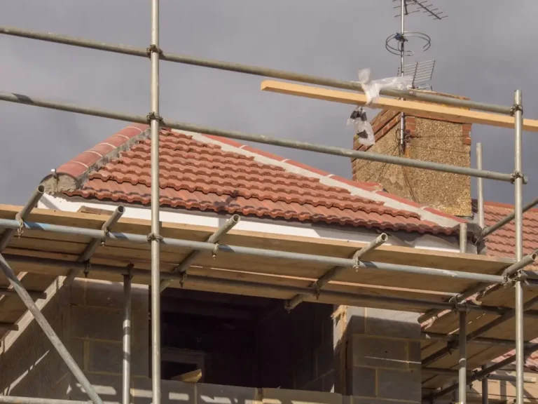 Building under construction with red roof tiles and scaffolding against cloudy sky