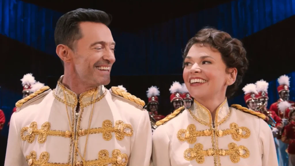 Hugh Jackman and Sutton Foster smiling at each other while wearing matching ornate white and gold stage costumes during a theatrical performance scene.