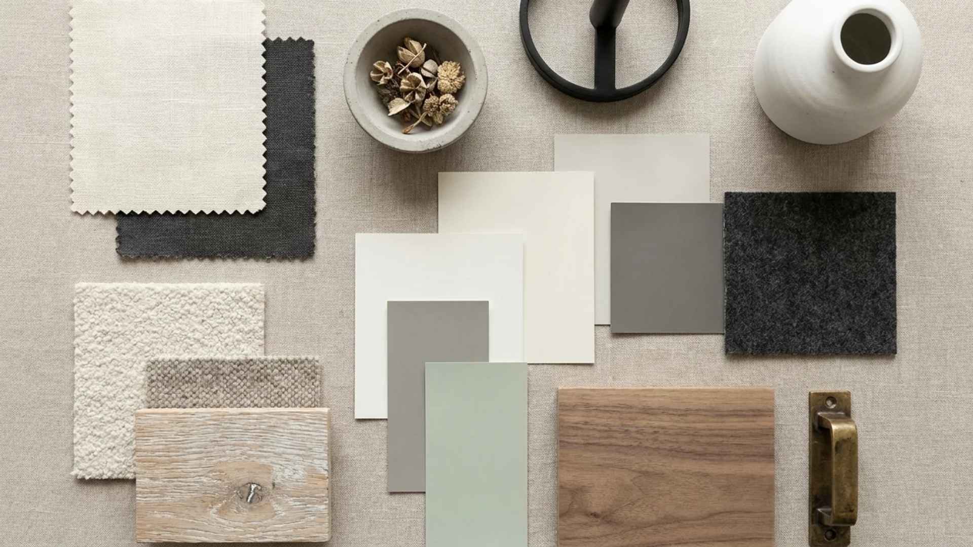 Flat lay mood board featuring fabric swatches, paint samples, a wood block, a white vase, and a brass handle on a gray surface.